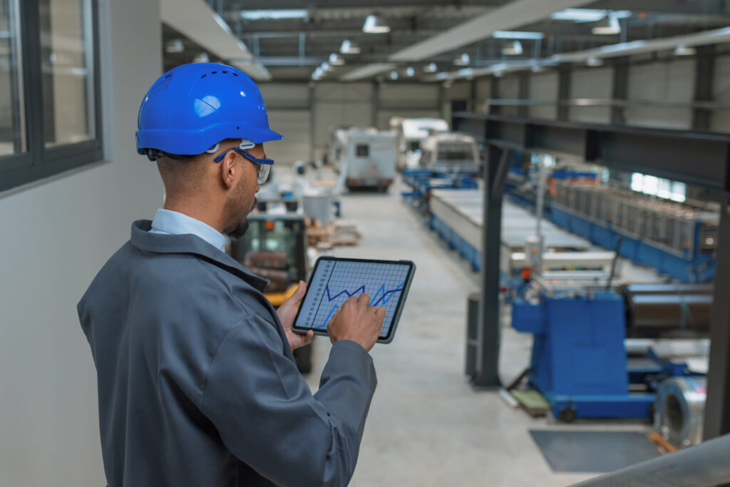 Young engineer programmer using tablet and graphs data to check factory machinery production and work procedure, rear view. Industry career concept.